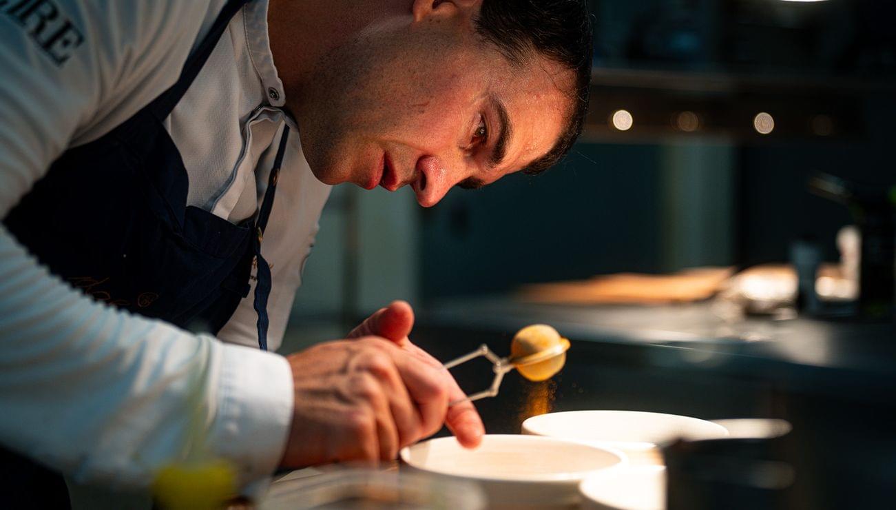 Chef carefully garnishing a dish in a professional kitchen under focused lighting