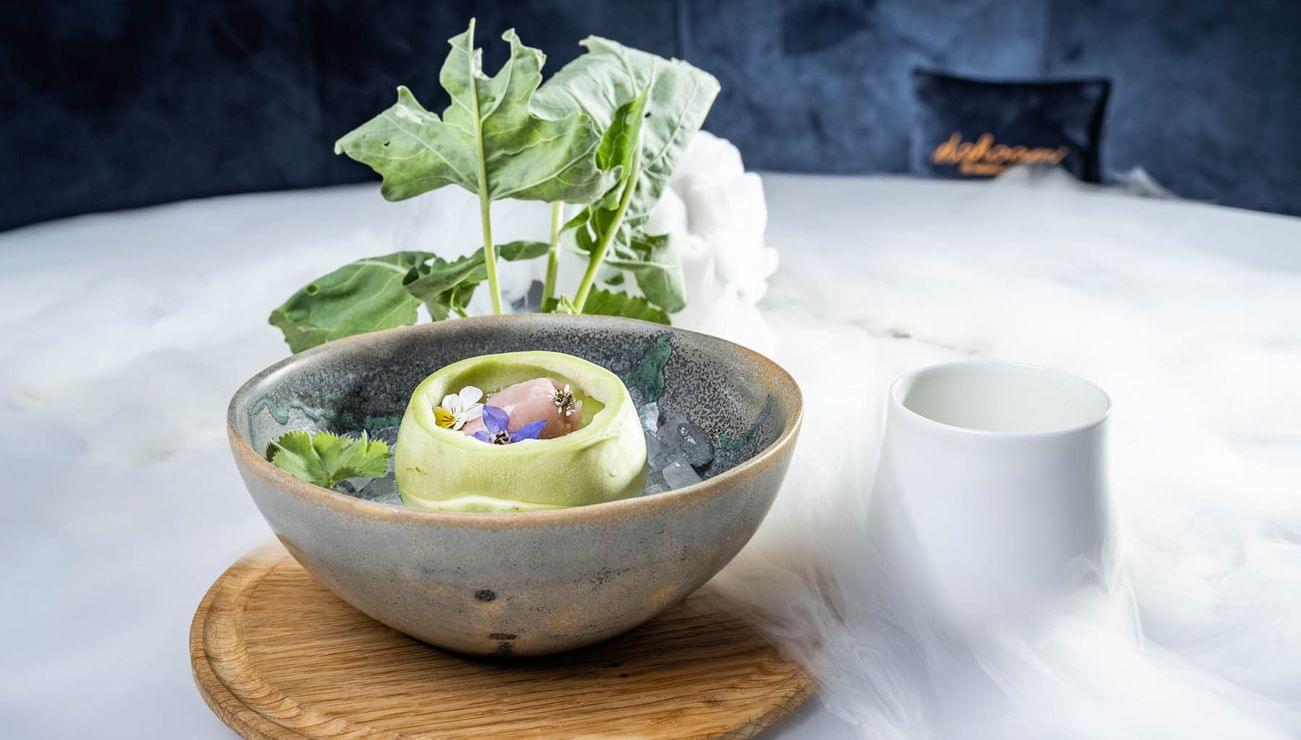 Gourmetgericht mit Blüten und grünem Gemüse in Keramikschale auf Holzbrett