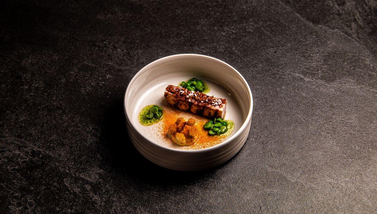 Gourmetgericht mit gegrilltem Fisch, grünen Erbsen und Gemüsecreme in weißem Teller