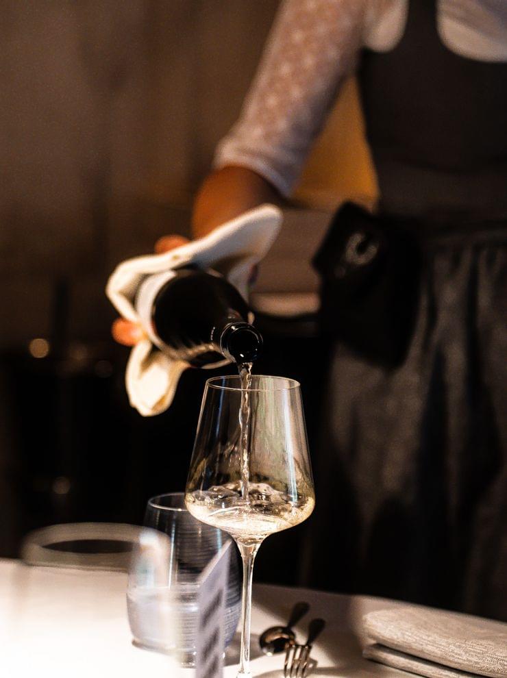 Kellnerin in Tracht schenkt Weißwein in ein Glas an einem eleganten Restauranttisch ein