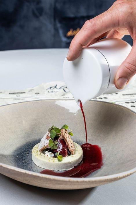 Gourmet-Dessert mit roter Sauce über Mousse und Mikrogrün garniert