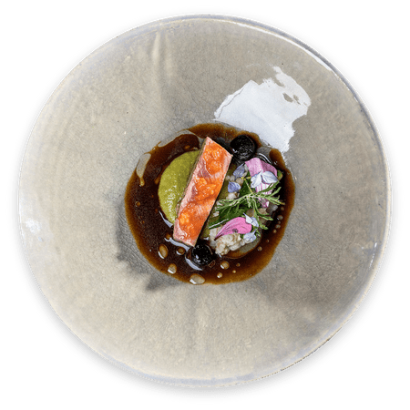 Gourmet salmon dish with sauce, herbs, flowers and puree on elegant ceramic plate