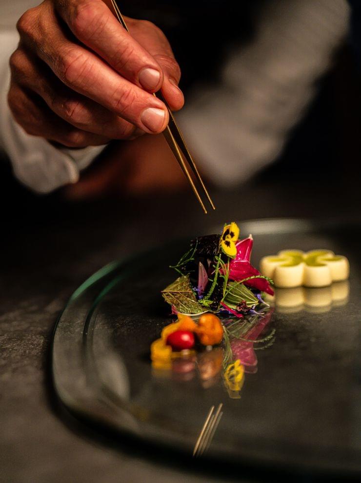 Koch richtet Gourmetgericht mit essbaren Blumen und bunten Garnierungen mit Pinzette an