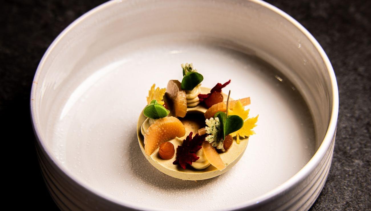 Fein dekoriertes Gourmet-Dessert mit Obst und essbaren Blüten auf Keramikteller
