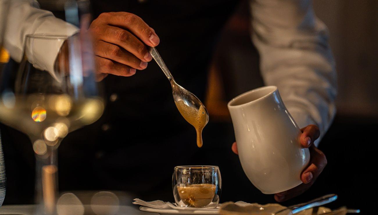 Barista löffelt cremigen Espresso in Glas auf elegant gedecktem Tisch