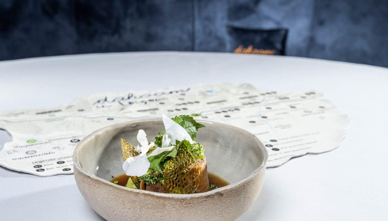 Gourmetgericht mit essbaren Blüten und Kräutern in einer Keramikschale auf weißer Tischdecke