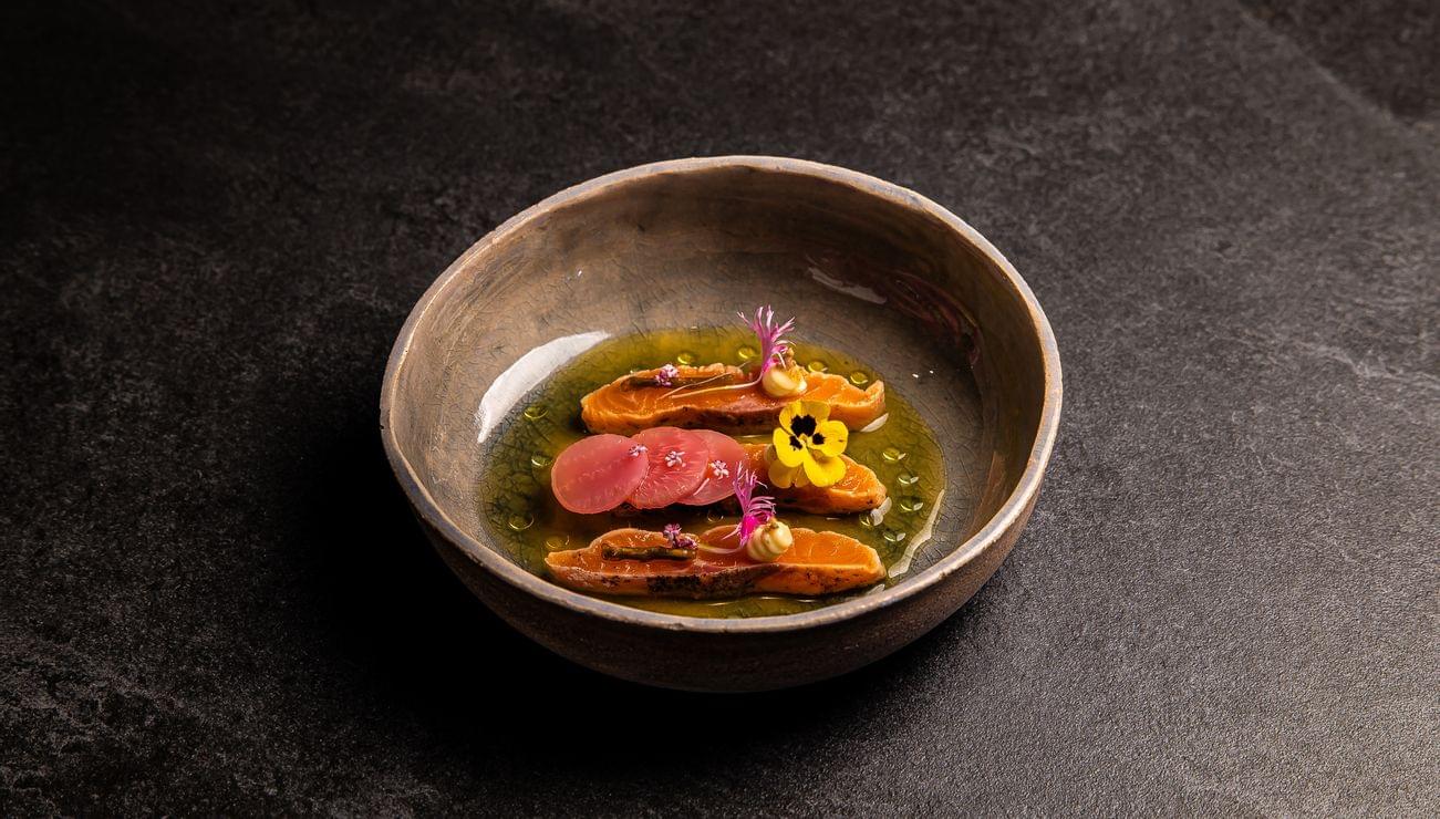 Gourmetgericht mit Lachs, Radieschen, Blüten und grüner Sauce in Keramikschale