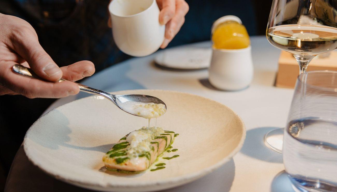 Koch richtet Gourmet-Lachs mit Sauce im Sternerestaurant an