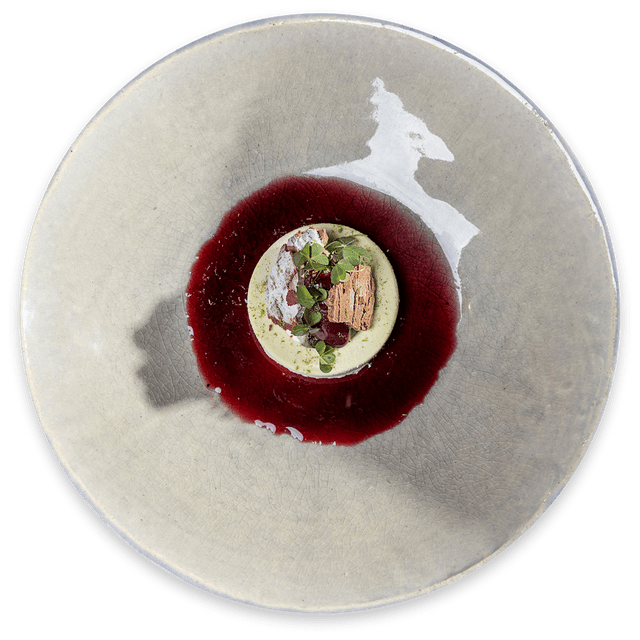 Gourmet dessert with green mousse, red berry sauce and edible garnish on ceramic plate