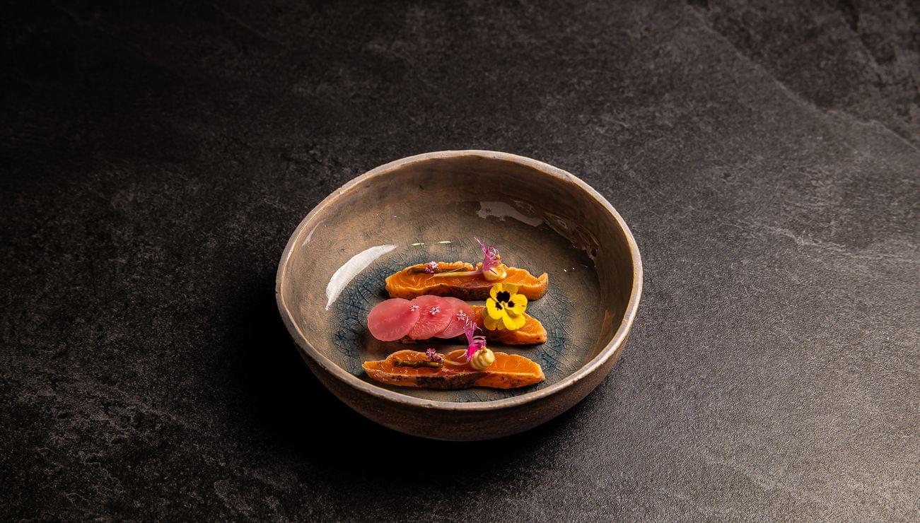 Gourmet plated sweet potato slices with pickled radish and edible flowers in ceramic bowl