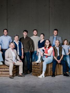 Mehrgenerationenfamilie steht und sitzt vor grauer Wand auf Holzkisten