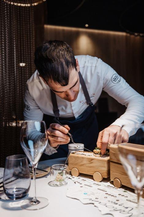 Chef plating gourmet dish on wooden toy train in fine dining restaurant